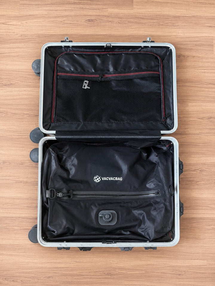 Open and empty suitcase with black interior on a wooden surface, featuring the VacVacBag inside of it.