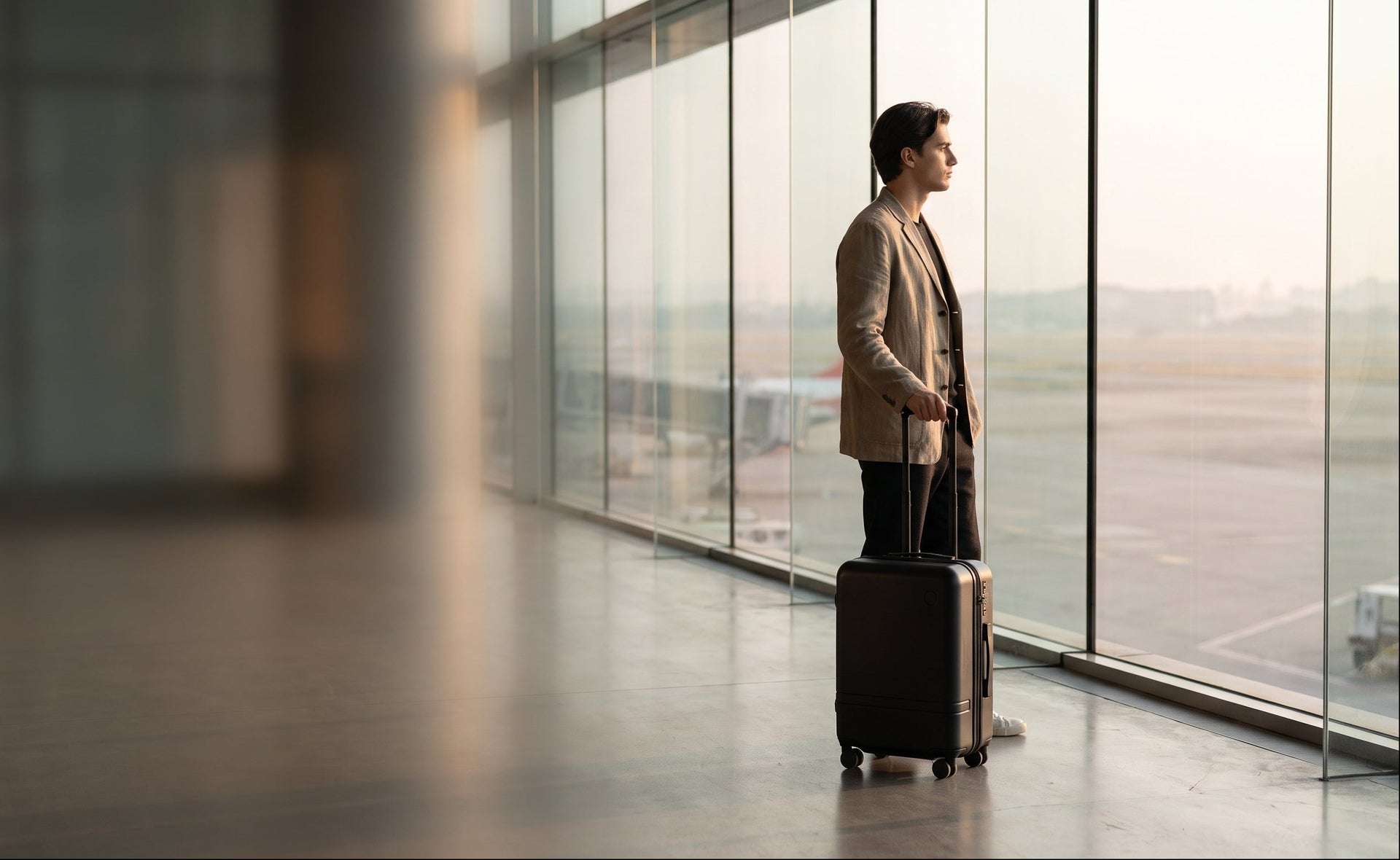 Person with a suitcase standing by large windows at an airport. The suitcase contains 2 VacVacBags.